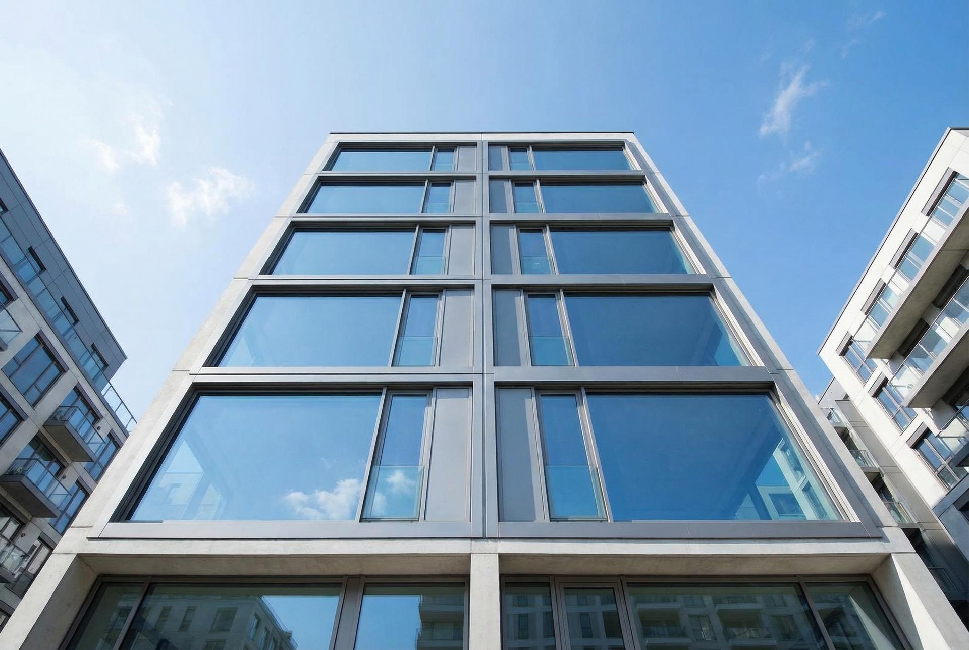Edificio residencial moderno con ventanas reflejando el cielo azul, representando la vivienda estable y urbana